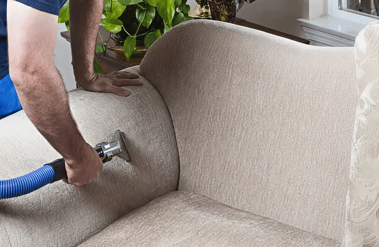 Professional upholstery cleaner deep-cleaning a fabric sofa with a handheld extraction tool and hose, Chicago, IL.